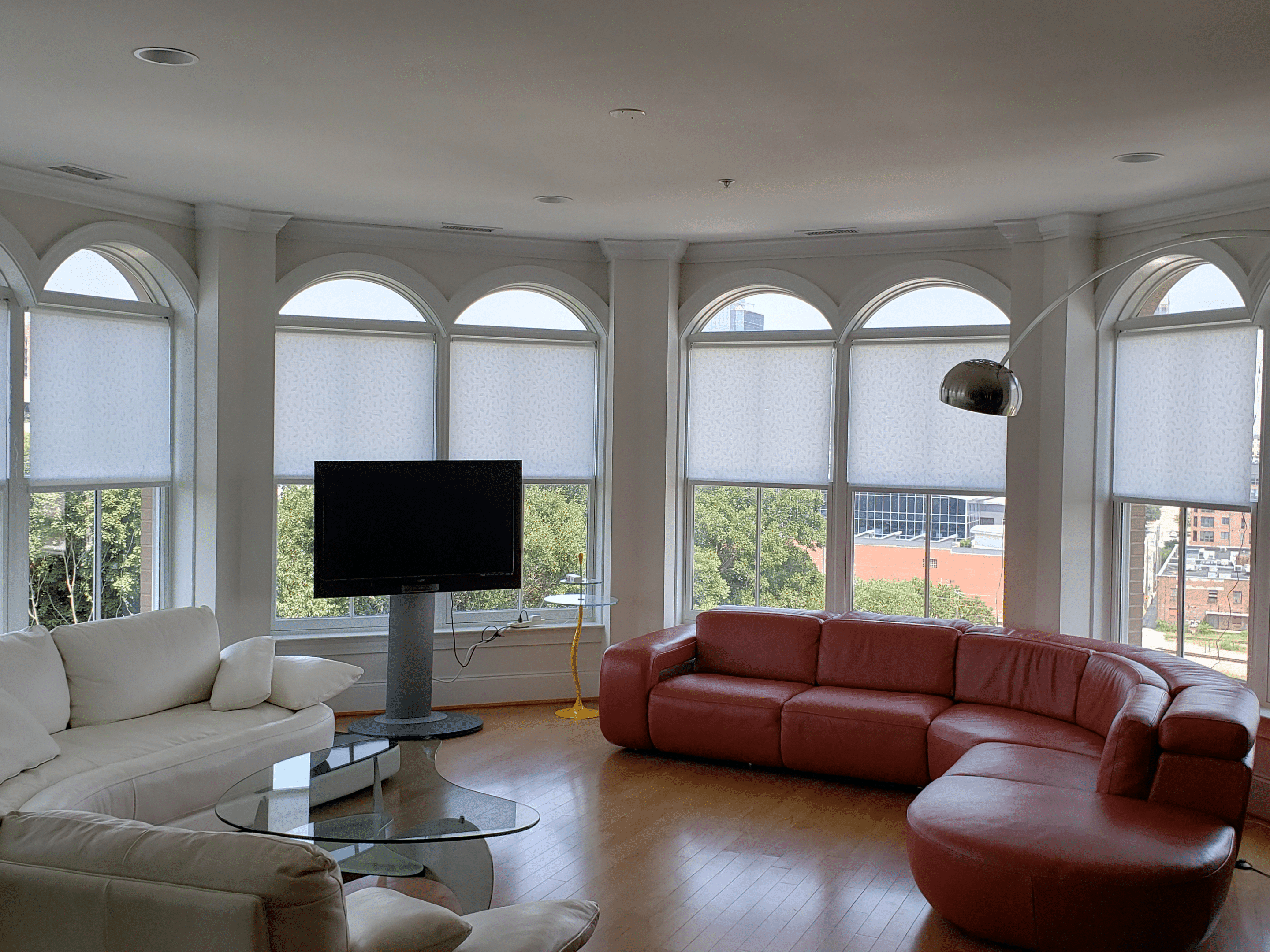 Sleek roller shades filtering in natural light into a great room with a red wrap around couch,